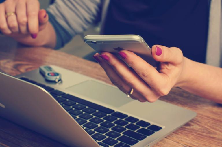 Hand hält Smartphone neben Laptop